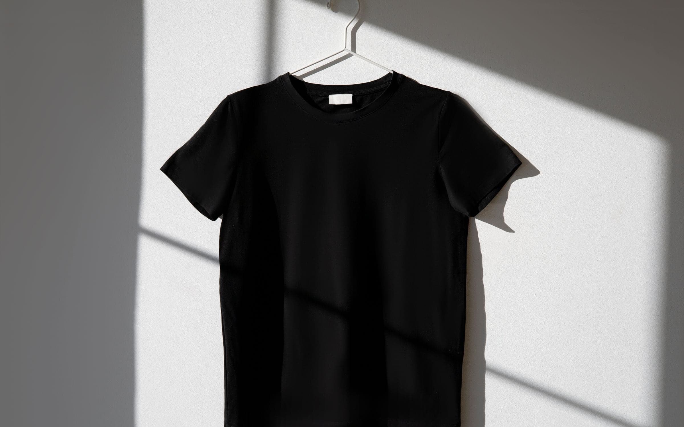 Finished black T-shirt on a hanger, catching sharp window-light shadows